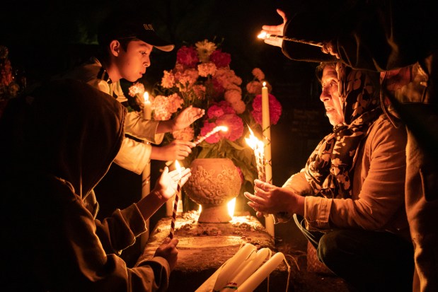 People hold candles over a tomb decorated with flowers at a cemetery in Atzompa, Mexico, late Tuesday, Oct. 31, 2023. In a tradition that coincides with All Saints Day on Nov. 1 and All Souls Day on Nov. 2, families decorate graves with flowers and candles and spend the night in the cemetery, eating and drinking as they keep company with their dearly departed. (AP Photo/Maria Alferez)